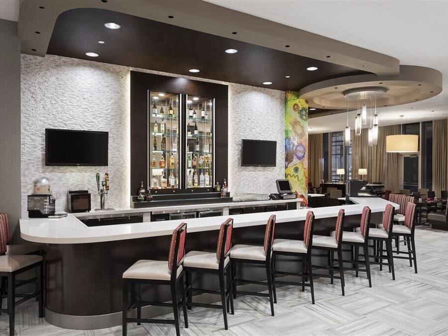 Zona de bar moderna con una barra larga, varios taburetes y una pantalla de televisión.