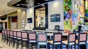 Un área de bar moderna con una barra larga, varios taburetes y un mural colorido en la pared.