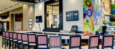 A modern bar area with a long counter, multiple bar stools, and a colorful mural on the wall.