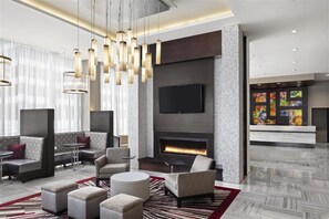 A modern lobby with seating areas, a fireplace, and a flat-screen TV mounted on the wall. - Cambria Hotel & Suites - White Plains Downtown (White Plains)