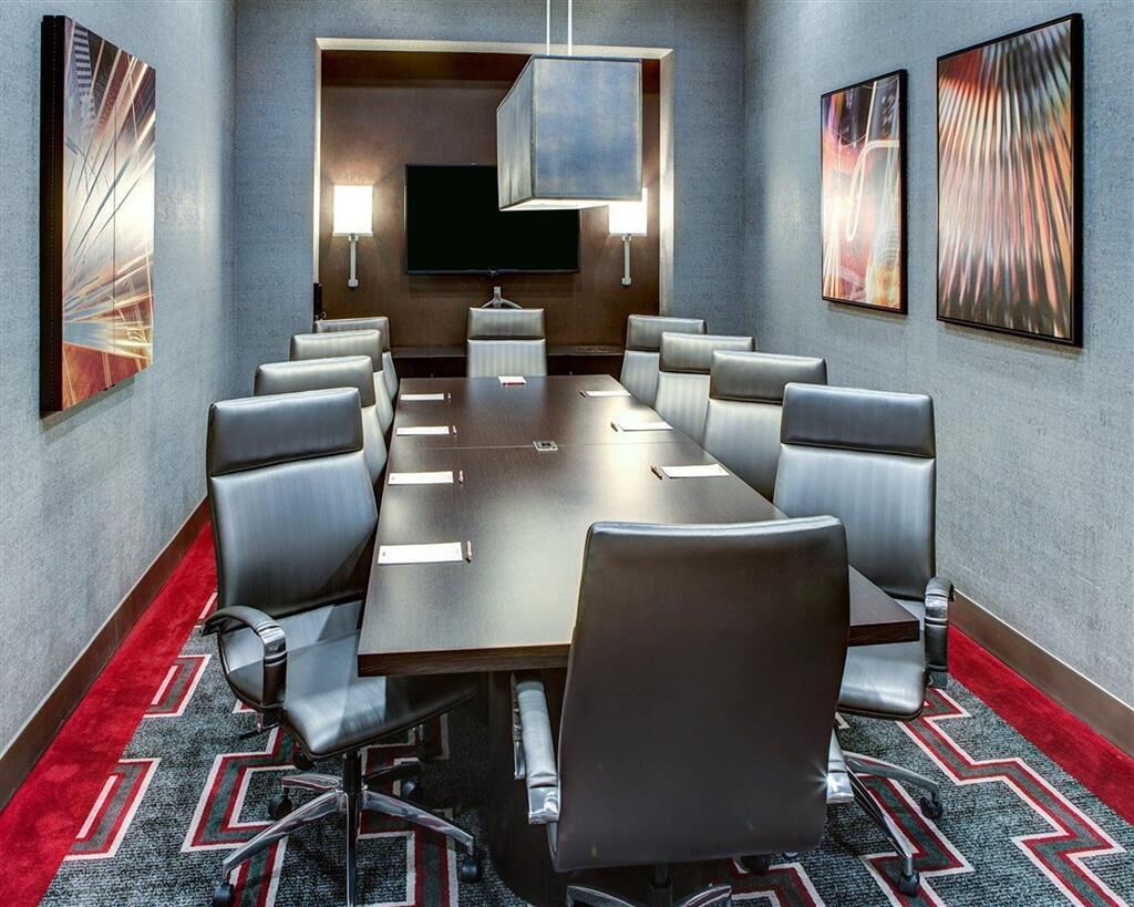 Un salón de conferencias con una mesa larga, varias sillas, un televisor de pantalla plana y obras de arte en las paredes.