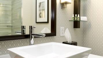 A modern bathroom with a large rectangular sink, a mirror, and a glass shelf with toiletries.
