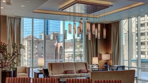 Um hall de hotel moderno com um sofá grande, área de refeições e amplas janelas com vista para a cidade.