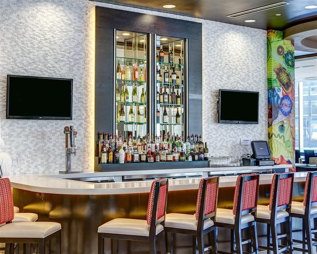 A bar area with a counter, multiple shelves of bottles, and bar stools.