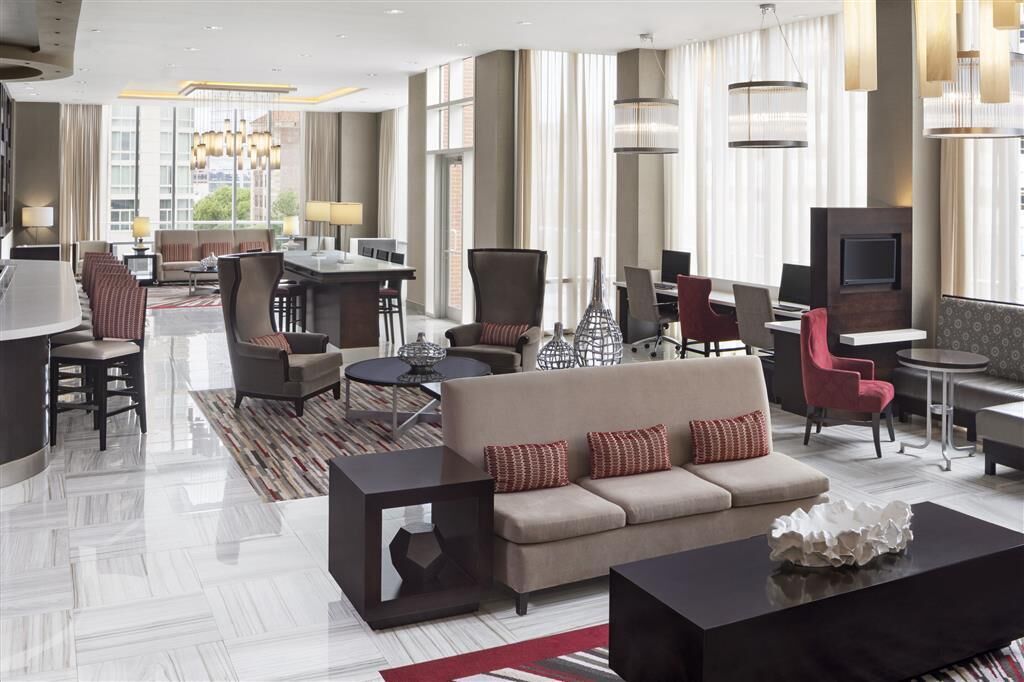 A modern hotel lobby with a sofa, chairs, a dining area, and a TV.