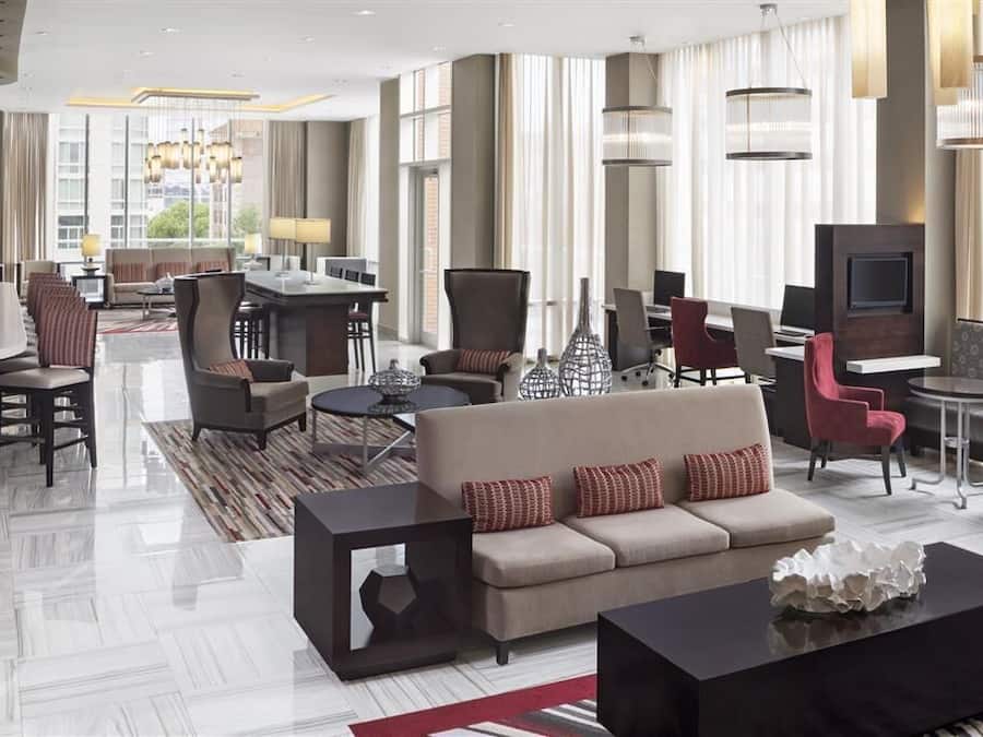 A modern hotel lobby with a sofa, chairs, a dining area, and a TV.