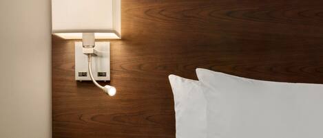 Un lit bien fait, avec du linge de lit blanc, une tête de lit en bois et une lampe de chevet.