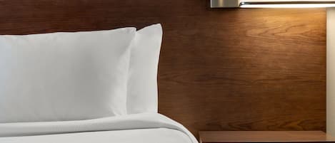 A neatly made bed with white linens, a wooden headboard, and a bedside table with a drawer.