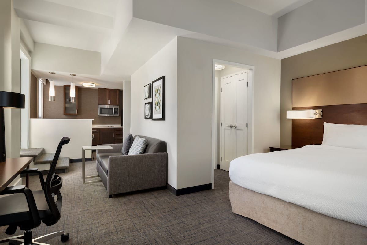 Een hotelkamer met een bed, een bureau, een stoel, een bank, een magnetron en een deur naar de badkamer.