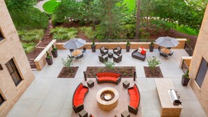 Un espace extérieur circulaire aménagé avec des sièges, comprenant un foyer, des canapés et des fauteuils, ainsi qu’un coin barbecue.