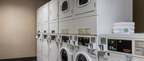 A laundry facility with multiple washing machines and dryers, control panels, and a stack of towels.