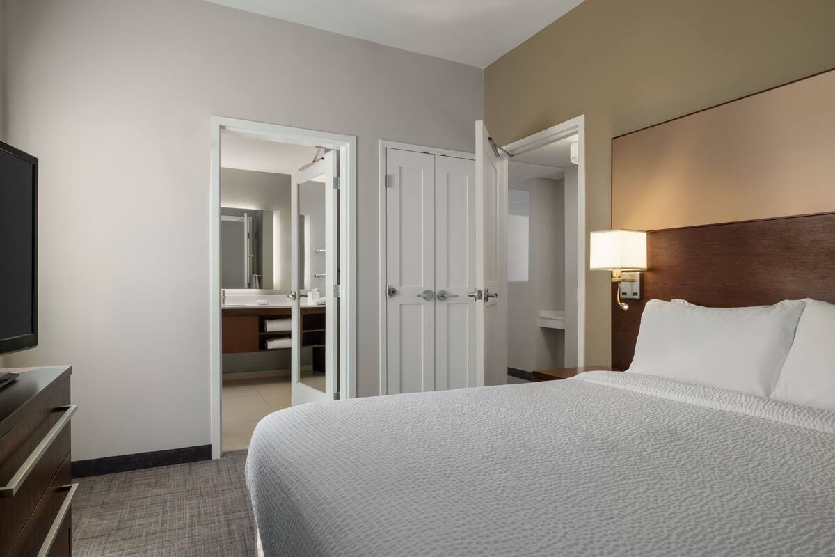 Een hotelkamer met een bed, een televisie, een kledingkast en een badkamer zichtbaar door een open deur.