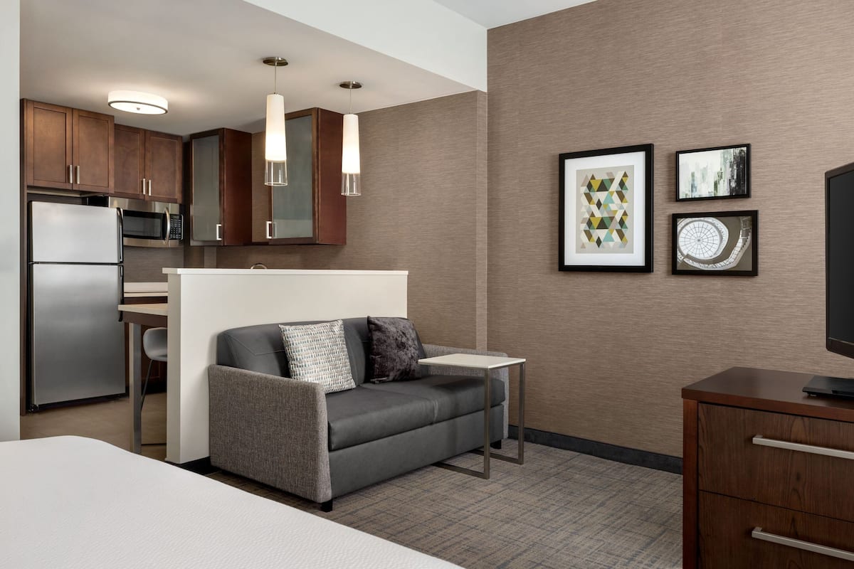Een moderne hotelkamer met kitchenette, een grijze bank met plaid, een eettafeltje en kunst aan de muur.
