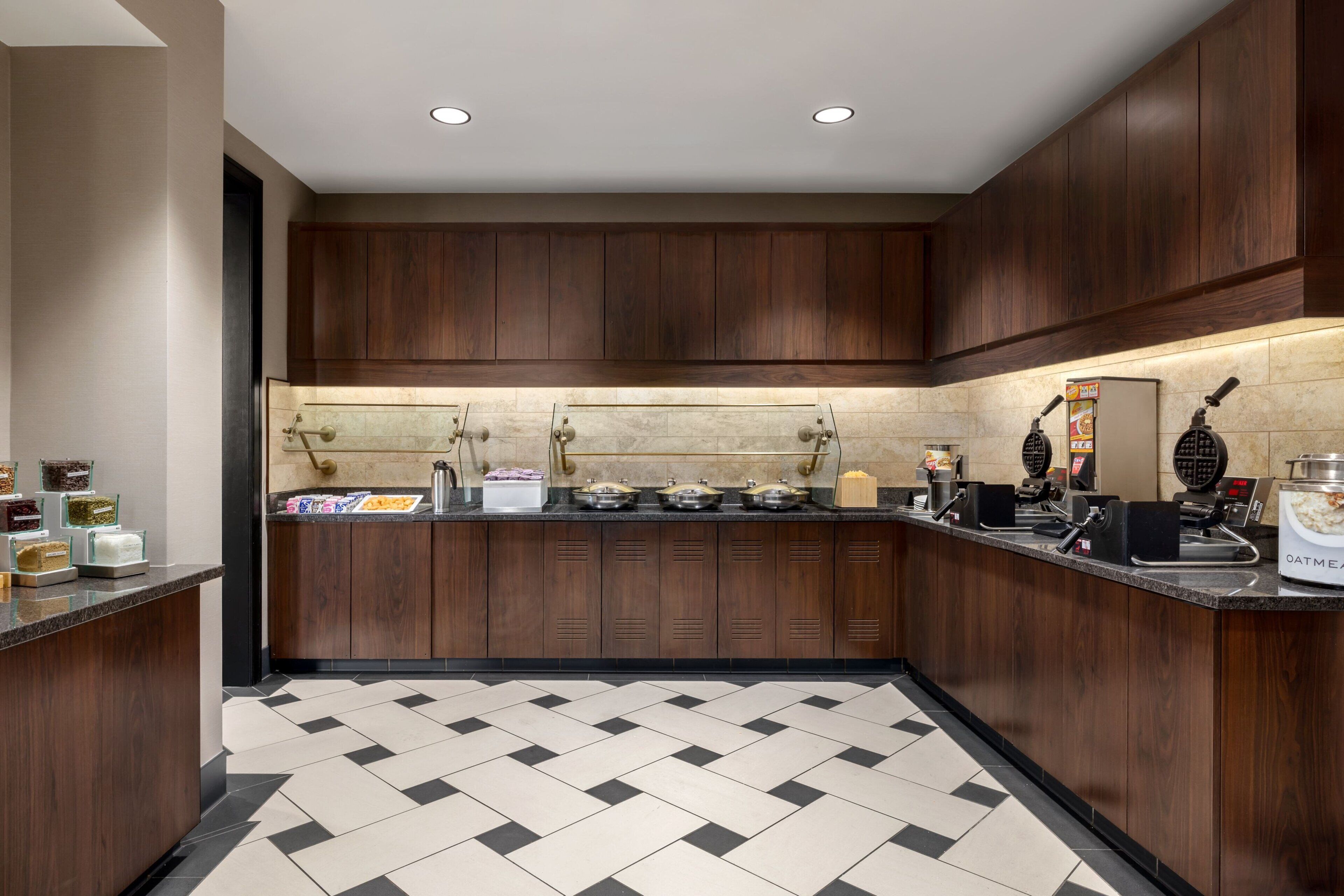 Una cocina moderna con armarios de madera, piso de baldosas blanco y negro, y varios electrodomésticos.