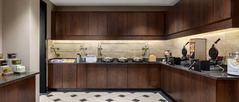 Una cocina moderna con armarios de madera, piso de baldosas blanco y negro, y varios electrodomésticos.
