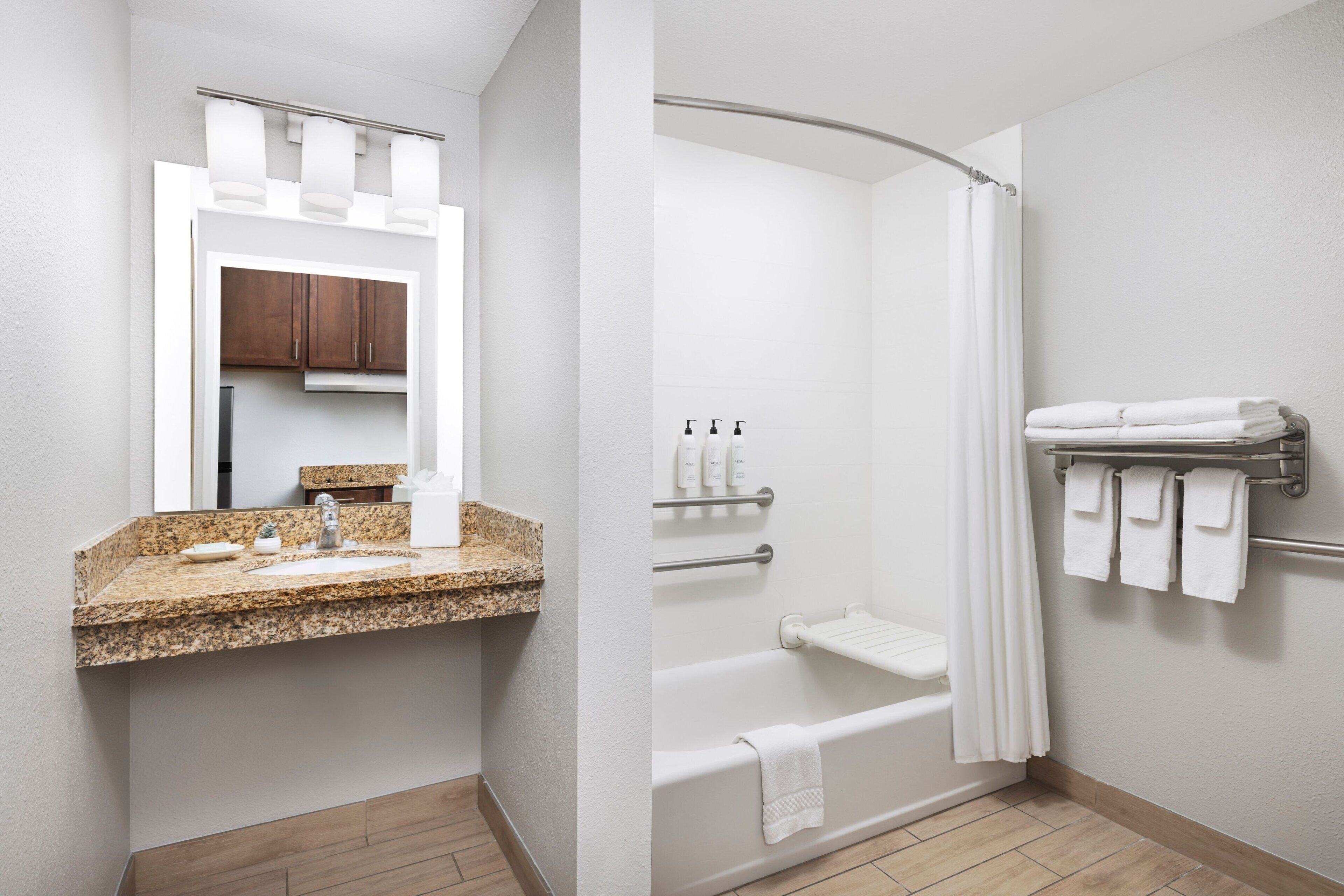 A bathroom with a granite countertop sink, a mirror, a shower with a curved glass door, and a towel rack with folded towels.