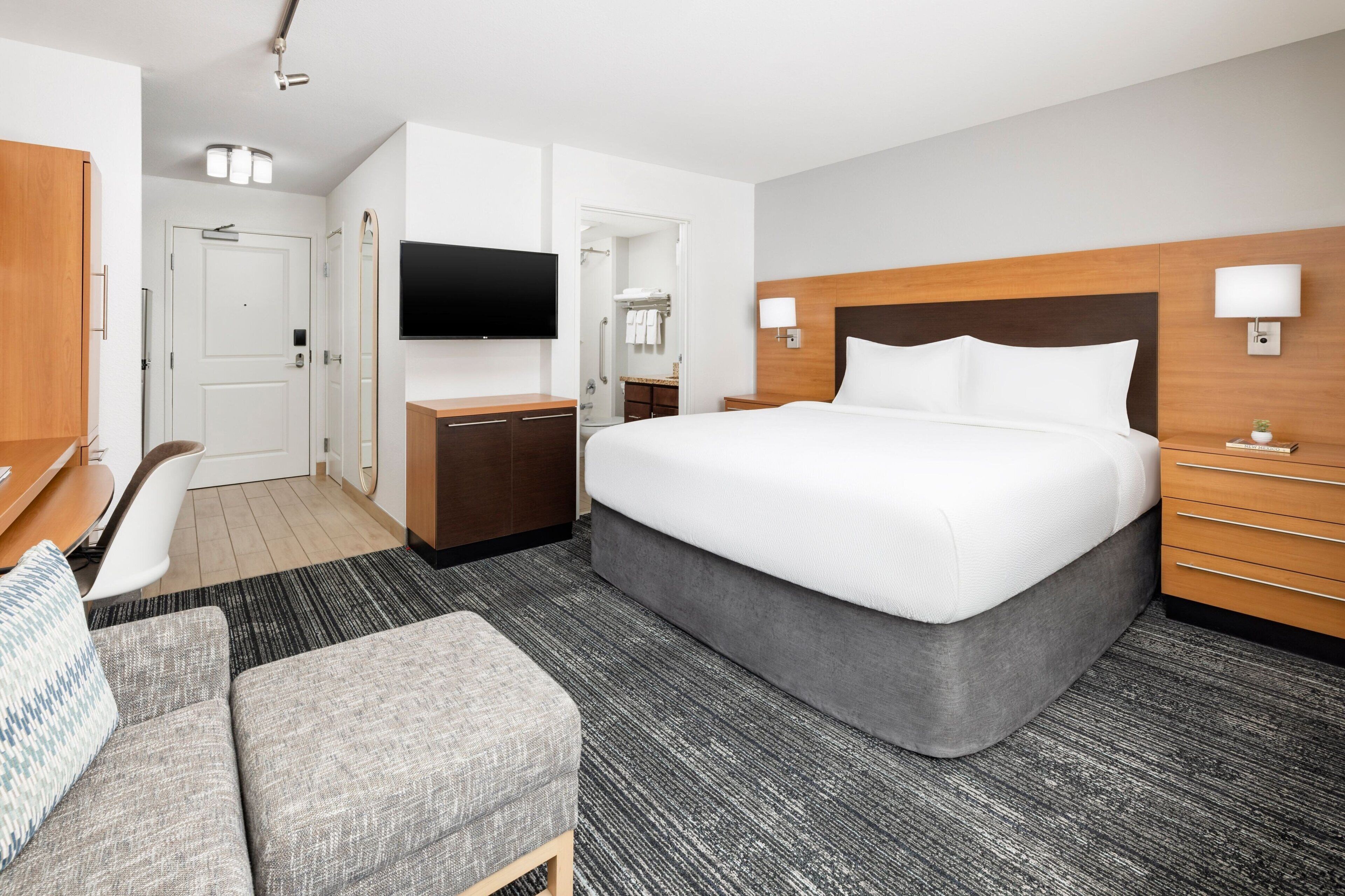 A hotel room with a large bed, a desk, a TV, a wardrobe, and a bathroom visible through an open door.
