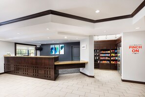 A modern reception area with a dark wood reception desk, a large window, and a wall-mounted artwork. - TownePlace Suites by Marriott Roswell (Roswell)