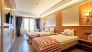 A hotel room with two beds, a desk, a chair, a TV, and a window with curtains. - May Park Hotel (Izmir)