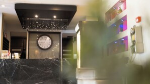 A lobby with a marble reception desk, a wall clock, and a staircase with a red accent. - May Park Hotel (Izmir)