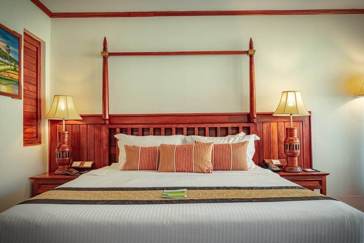 A four-poster bed with a wooden headboard, two bedside tables with lamps, and a painting on the wall.