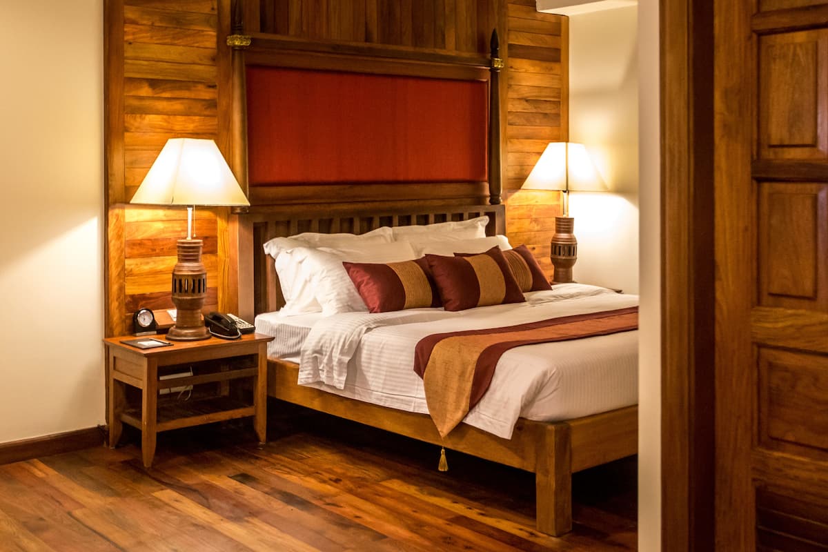 A wooden-framed bed with a red headboard, two bedside tables with lamps, and a telephone on the left table.