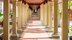 Un pasillo con techo de madera y columnas, que conduce a un espacio sombreado con plantas.