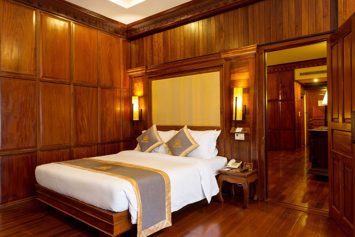 A large wooden-paneled bedroom with a bed, bedside tables, and a mirror.