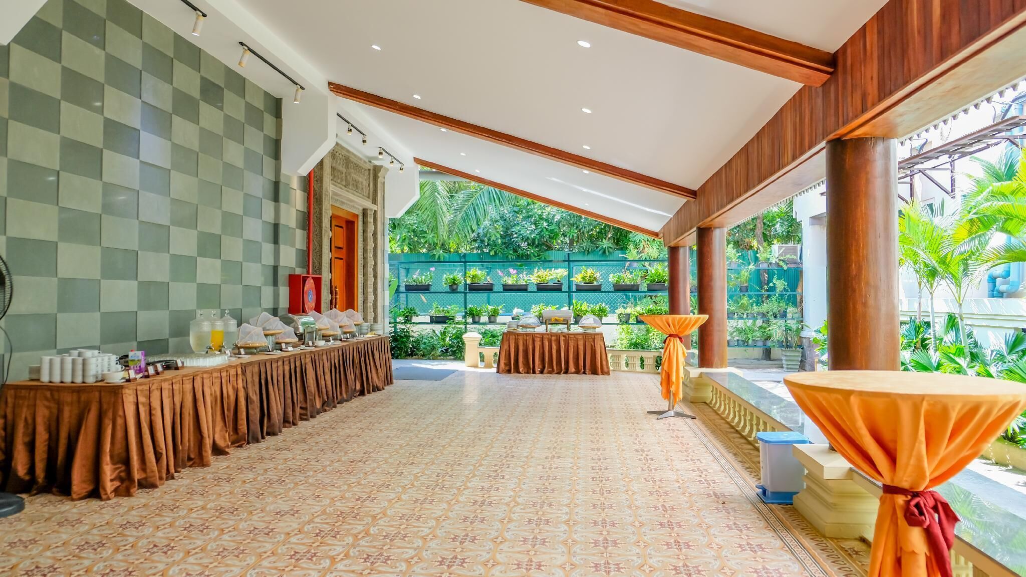 A spacious breakfast area with a long table, a buffet setup, and a view of a lush garden through large windows.