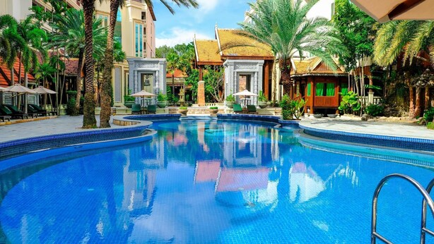 Una amplia piscina cristalina rodeada de palmeras y arquitectura tradicional.
