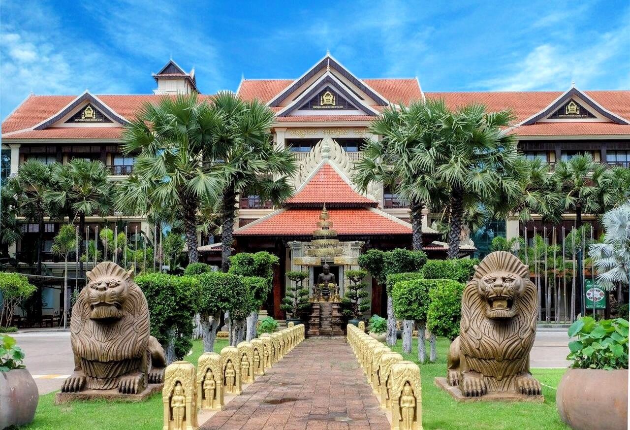 Un bâtiment traditionnel doté d’une entrée centrale, flanquée de deux statues de lions, et entouré d’un espace verdoyant bien entretenu.