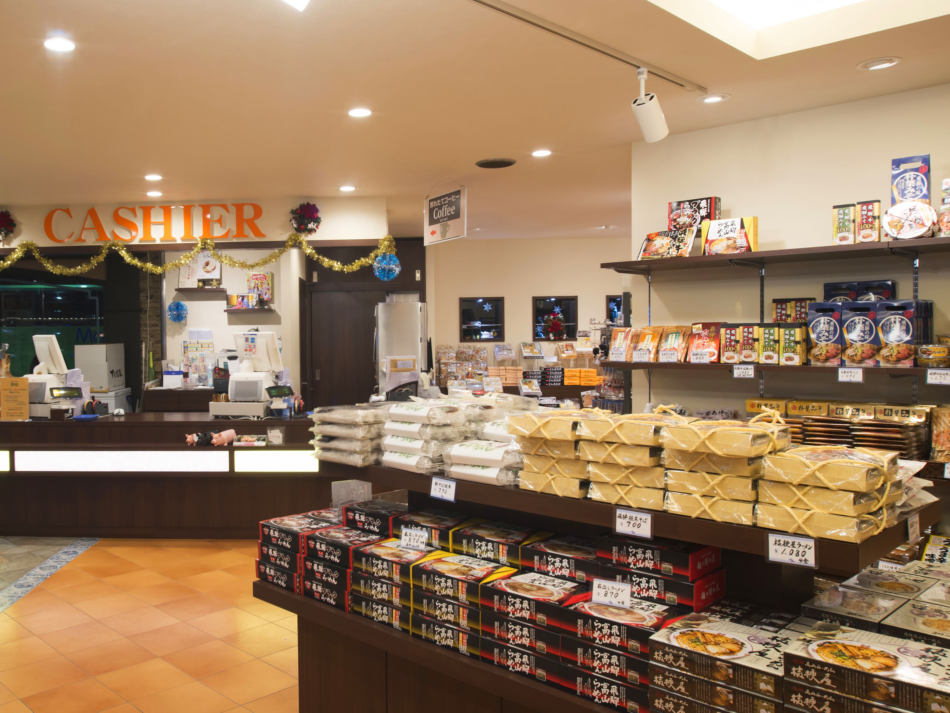 A store interior with a cashier counter, shelves stocked with packaged goods, and a tiled floor.