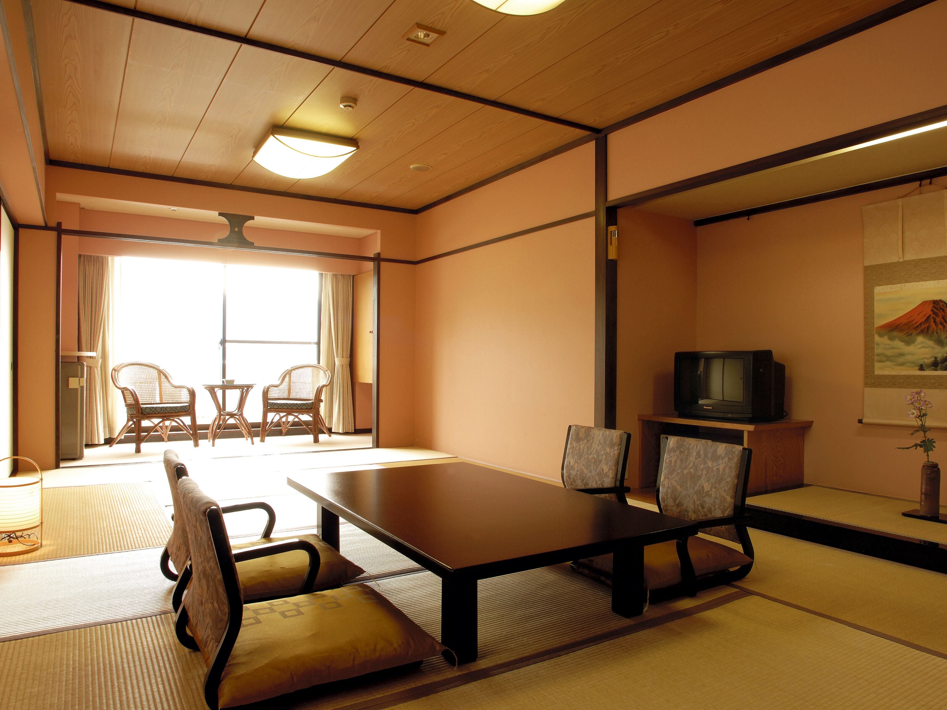 Una habitación tradicional japonesa con suelo de tatami, una mesa baja con sillas, un televisor y un cuadro en la pared.