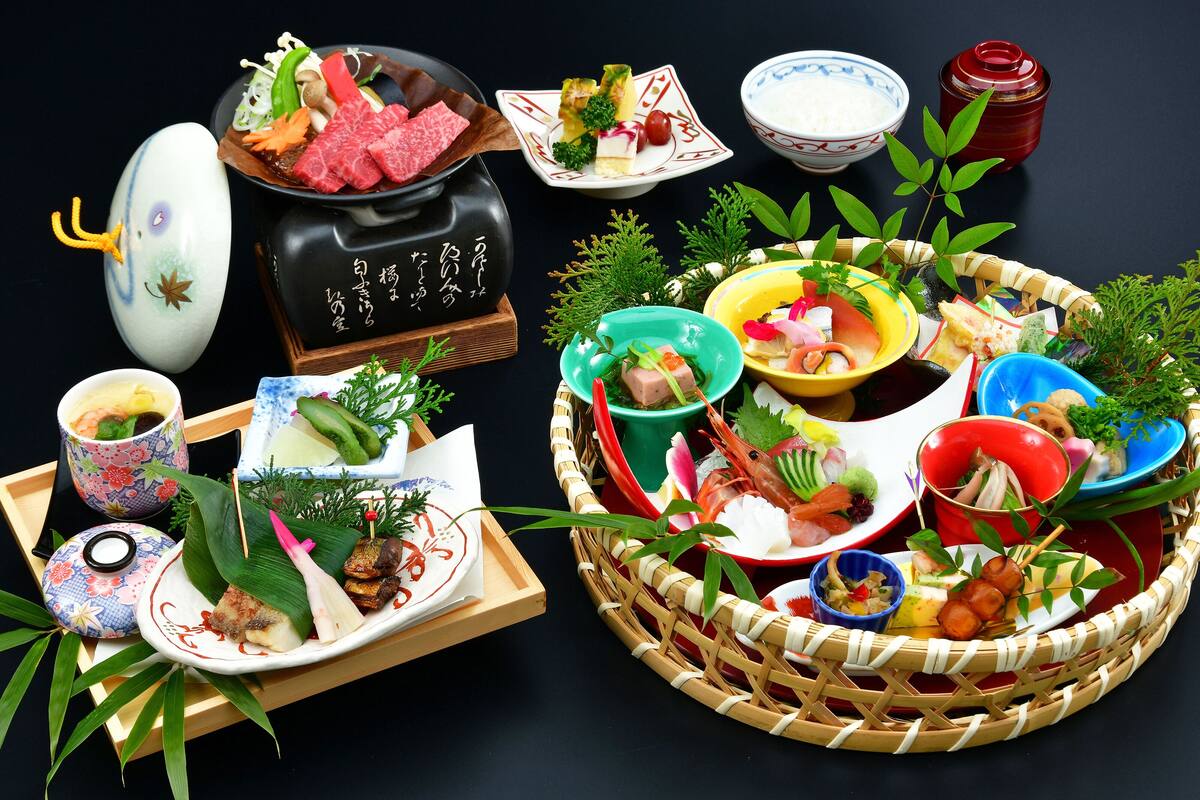 Variedad de platos japoneses dispuestos en una mesa, incluyendo sushi, sashimi y otras exquisiteces, con palillos y una tetera a la vista.
