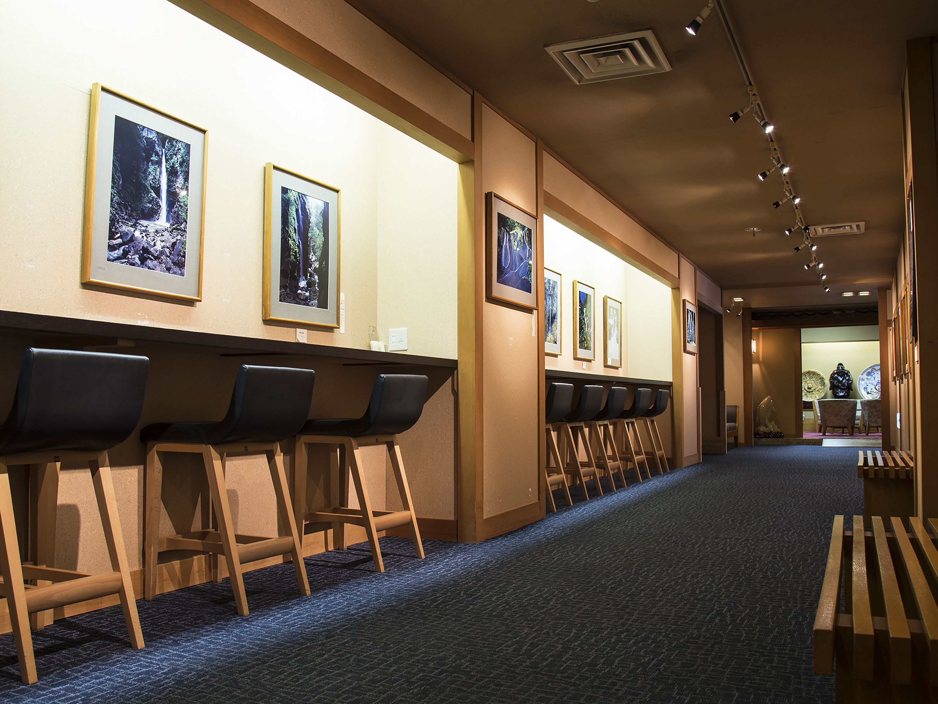 A hotel corridor with a row of bar stools, a carpeted floor, and framed pictures on the wall.