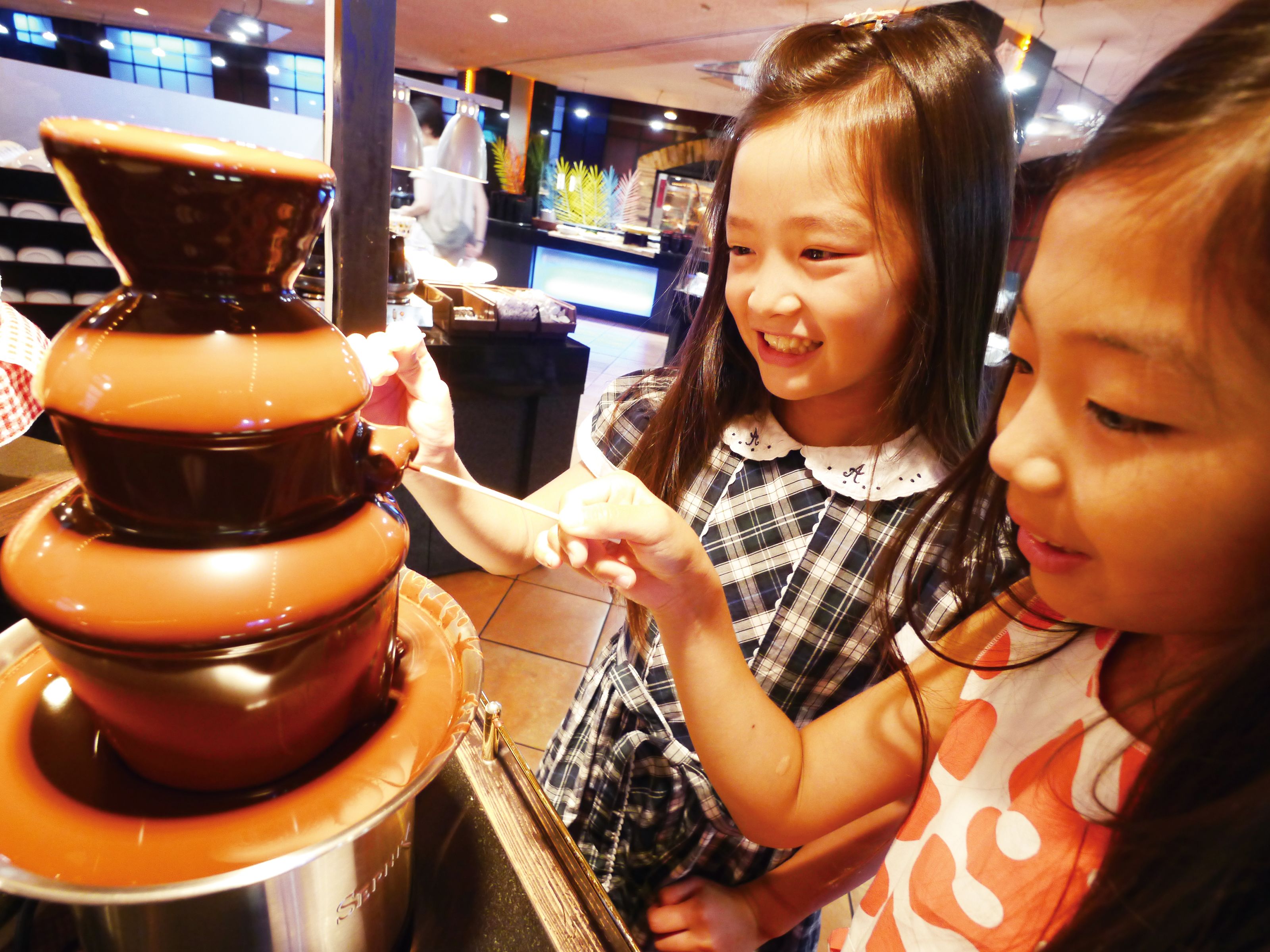Two children interacting with a large, multi-tiered chocolate fountain.