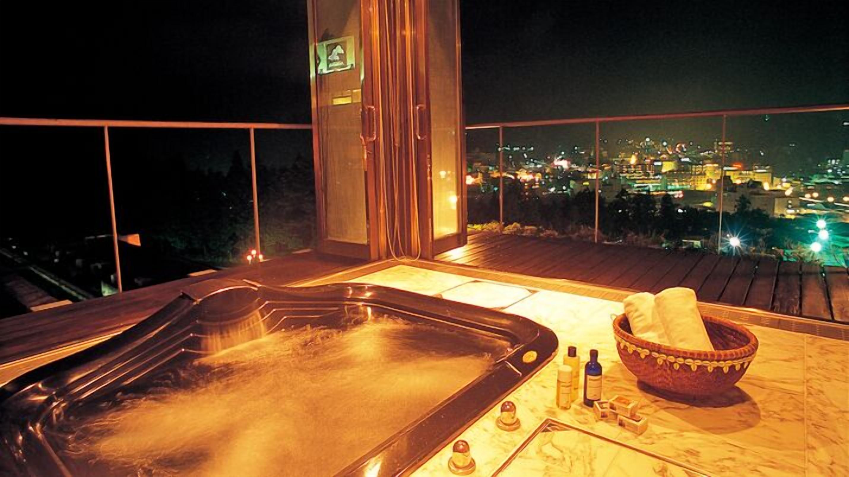 A hot tub on a balcony with a city view at night.