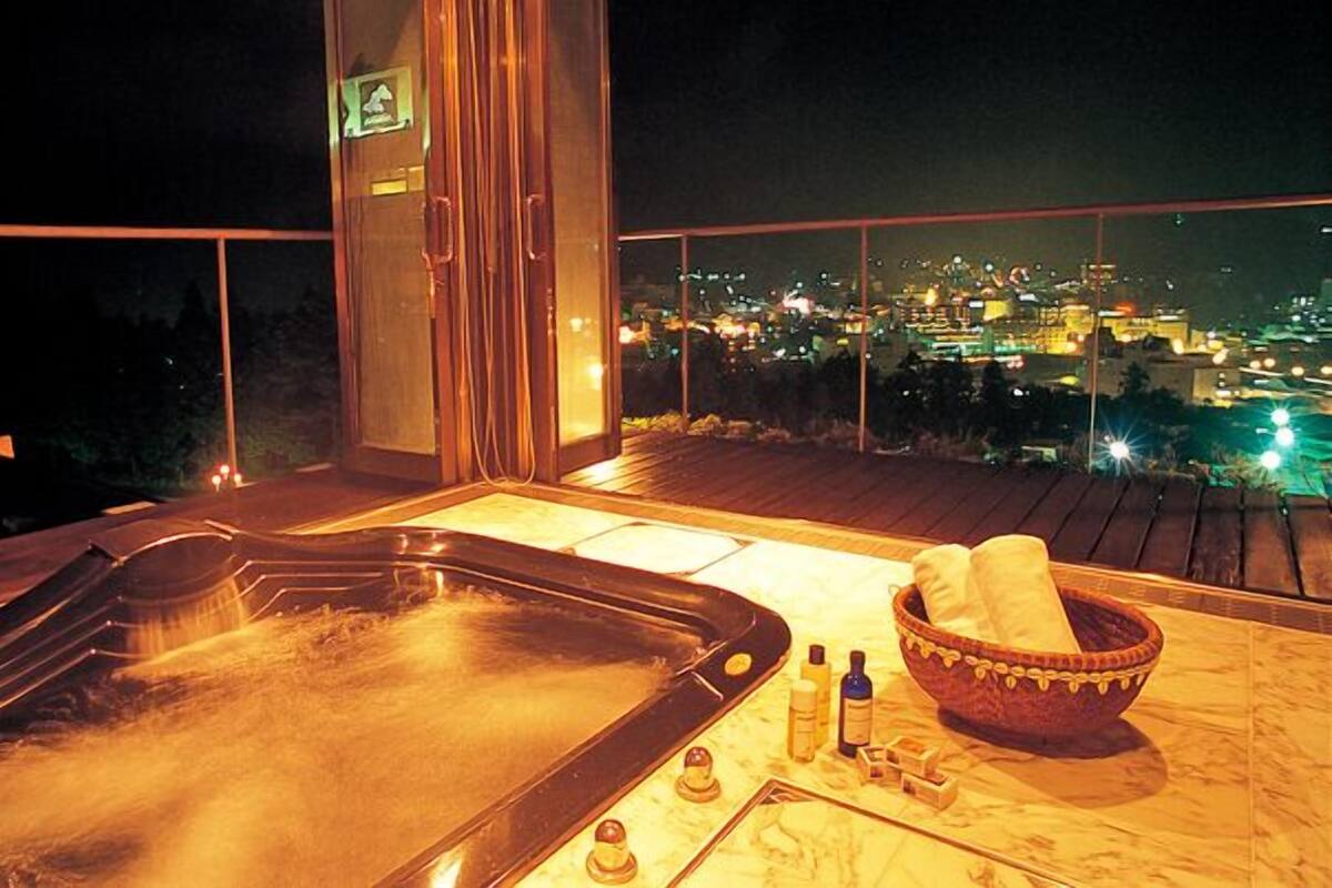Un jacuzzi en un balcón con vista a la ciudad de noche.
