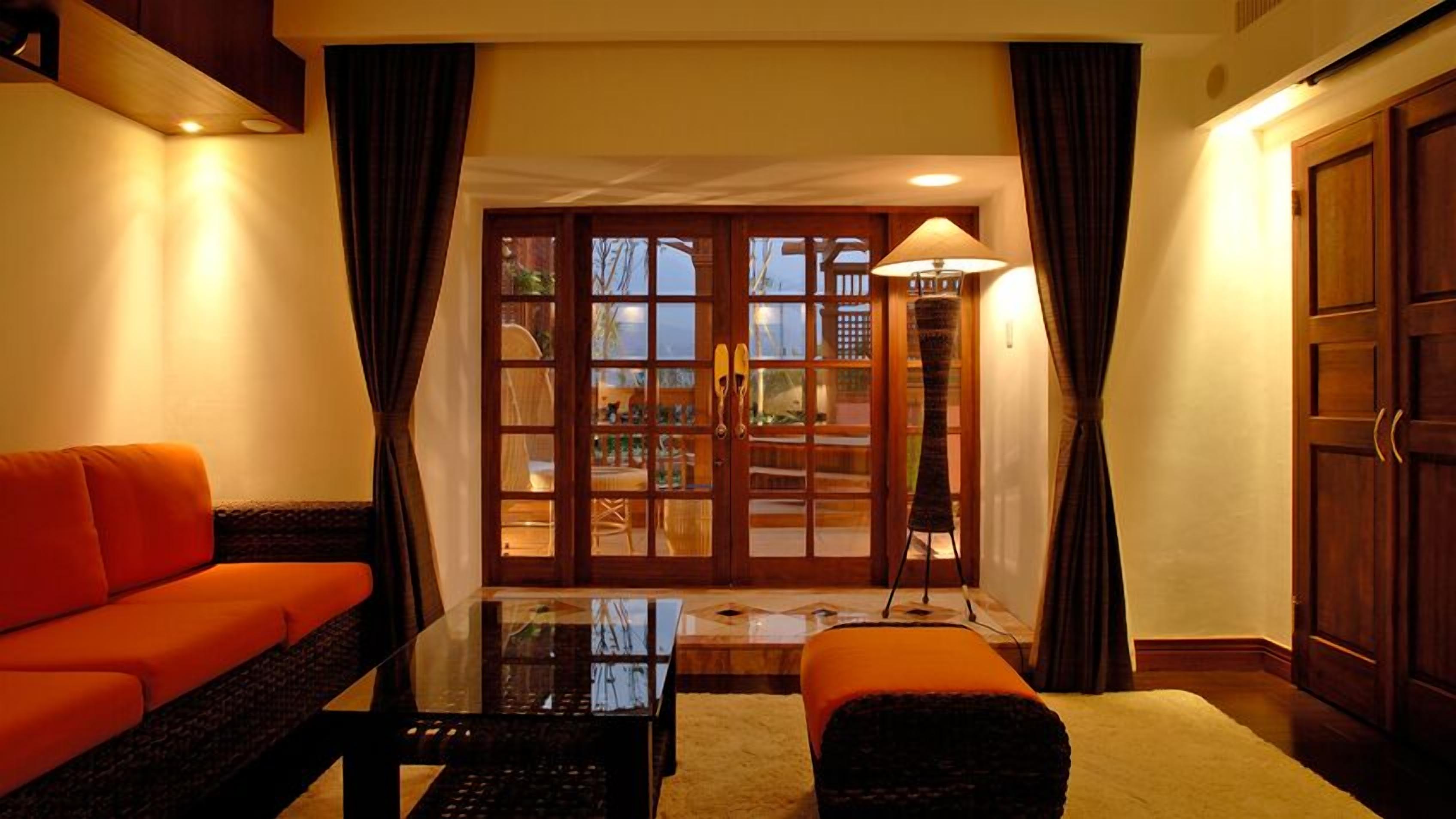 A room with a sofa, a table, a lamp, and a view through a glass door.