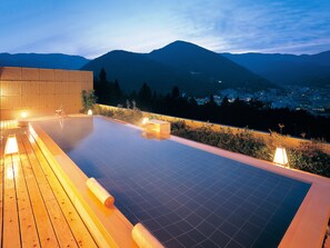 Une piscine à débordement située sur le toit, avec une terrasse en bois et des chaises longues, offrant une vue imprenable sur le paysage urbain et les montagnes.