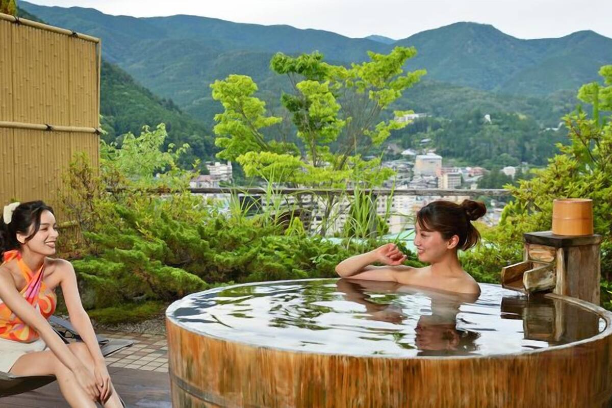 Dos personas sentadas junto a un jacuzzi con vistas a montañas y un paisaje urbano.
