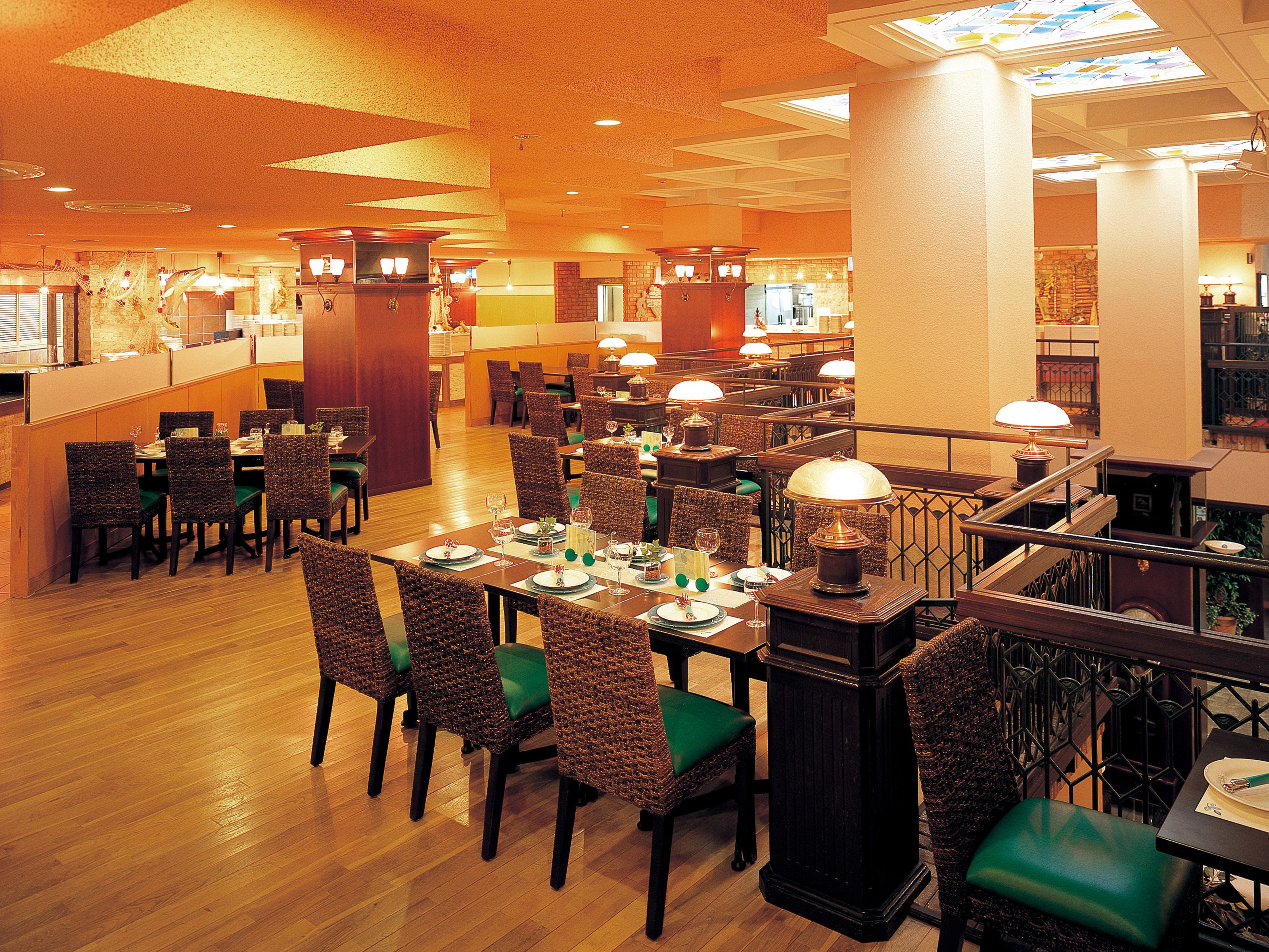 Un restaurante espacioso con varias zonas de comedor, pisos de madera y sillas con acolchado verde.