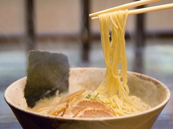 Un tazón de ramen con fideos que se levantan con palillos, una loncha de carne y alga marina.