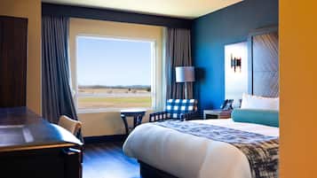 A hotel room with a large bed, a desk, a chair, a small table, a lamp, and a view of the outdoors.
