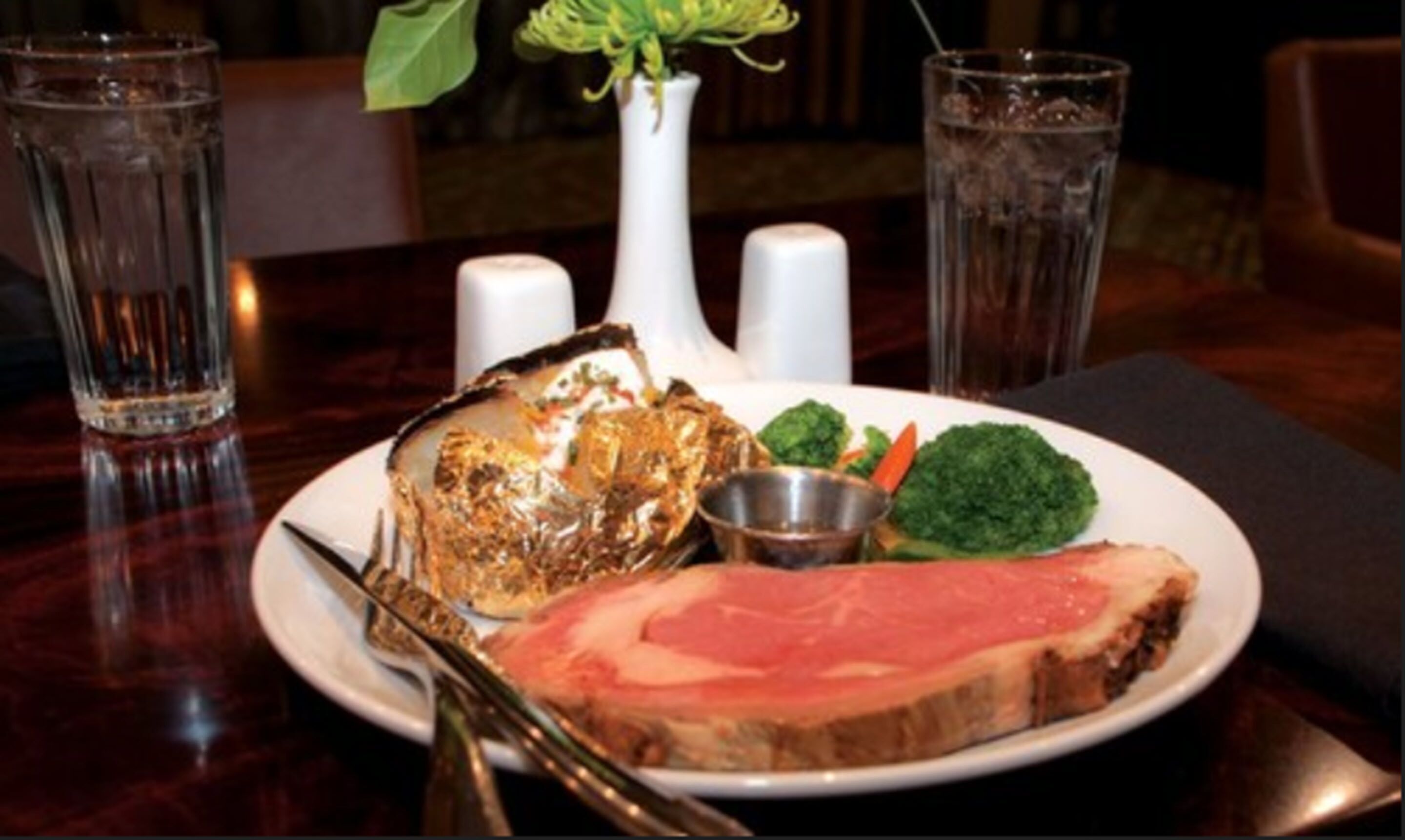 A plate with a slice of meat, a piece of fried food, and some vegetables on a table.