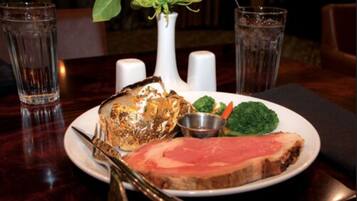 A plate with a slice of meat, a piece of fried food, and some vegetables on a table.