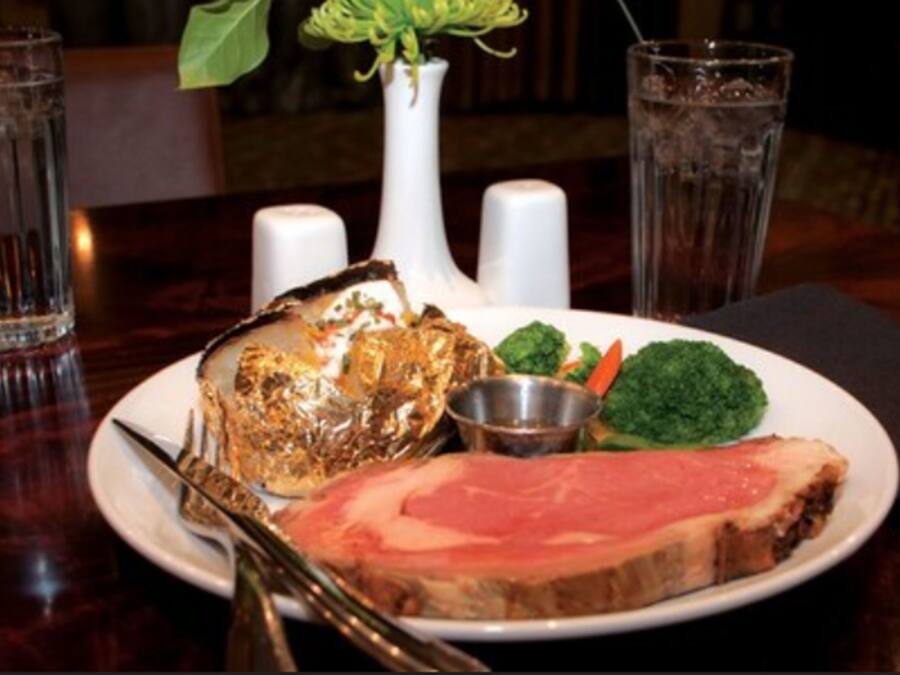 A plate with a slice of meat, a piece of fried food, and some vegetables on a table.