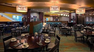 A hotel dining area with multiple tables, chairs, and a central seating area.