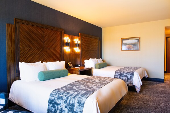 A hotel room with two beds, a wooden headboard, a bedside table with a lamp, and a framed picture on the wall.