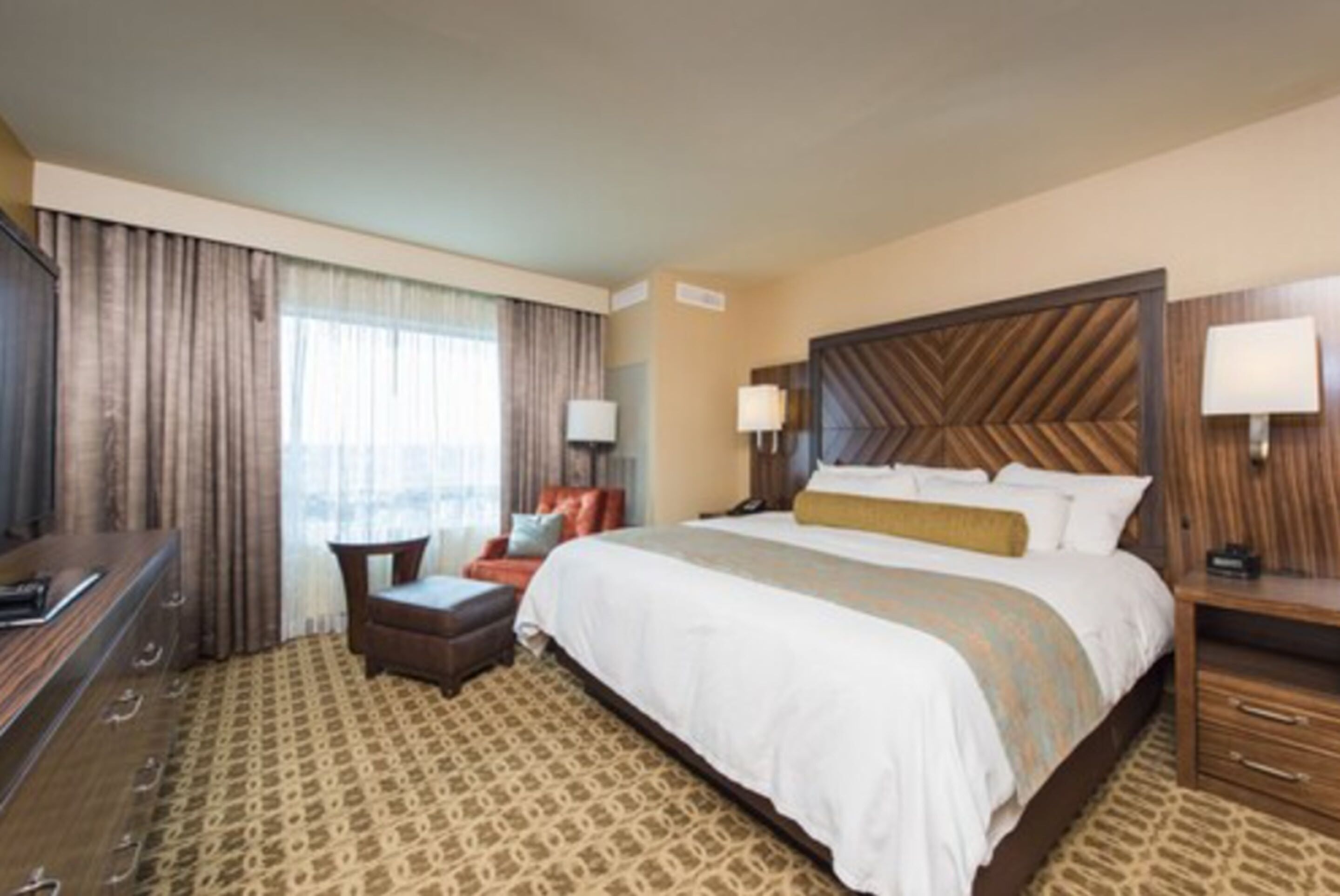 A hotel room with a large bed, a desk, a chair, a TV, and a window with curtains.